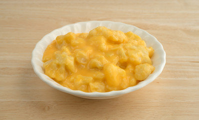 Serving of cauliflower with a cheese sauce in an old bowl atop a wood table top.