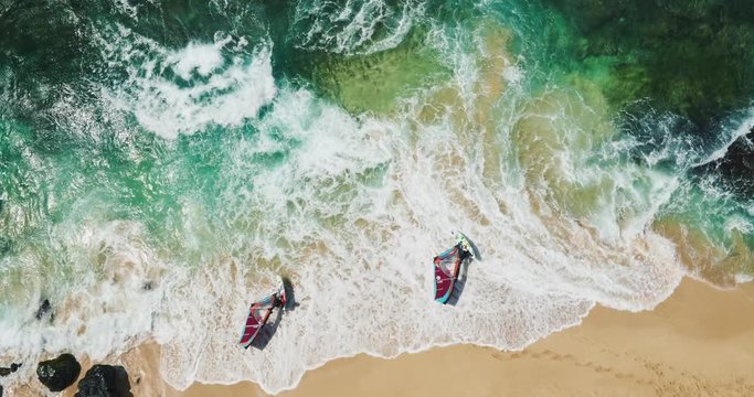 Aerial view of windsurfers launching from white sand beach into crashing surf
