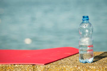 Pink sport mat and water bottle outdoor on sea shore
