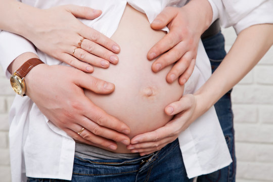 belly of a pregnant woman with her husband's hands