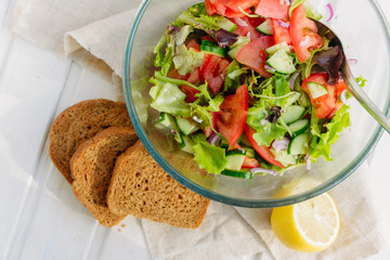 taste of vegetarian summer concept, salad of lettuce leaf, tomato, cucumber, onion, oregano with olive oil and lemon juice on white wooden background