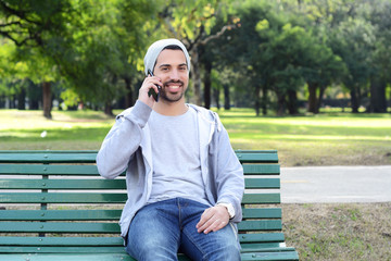 Fototapeta premium Young man talking on the phone sitting on park bench.