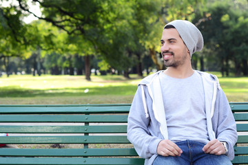Fototapeta premium Young latin man sitting on park bench.