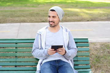 Obraz premium Young man using tablet sitting on park bench.