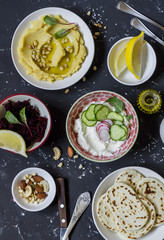 Snack table - hummus, beetroot sauce, cream sauce with vegetables, homemade tortillas. On dark stone background