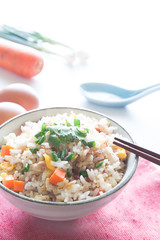 Bowl of fried rice, carrot and egg on pink fabric, spoon, chopst