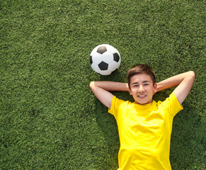 happy teenage boy with a soccer ball lying on the green lawn