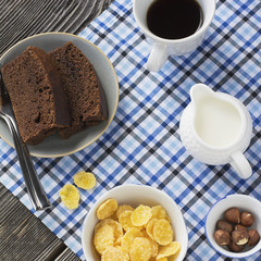Healthy breakfast. Cornflakes, milk, cup of black coffee and slice chocolate cake