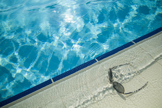 Sun glasses on the pool side and water reflection