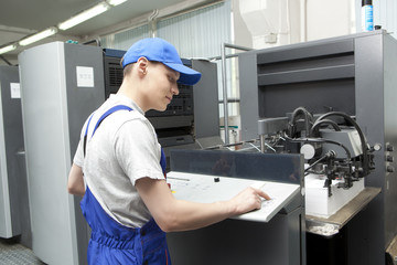 Young man in cap working on offset printing machine