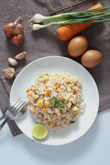 A dish of fried rice, carrot and egg on brown fabric, spoon, fol