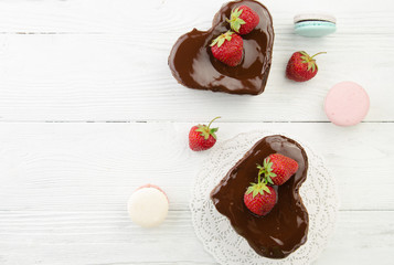 Heart cake and french macarons. Pieces of chocolate cake with fresh strawberry on wooden background. Top view.