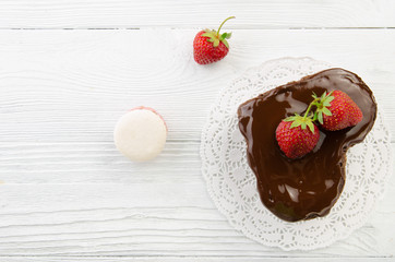Heart cake and french macarons. Pieces of chocolate cake with fresh strawberry on wooden background. Top view.