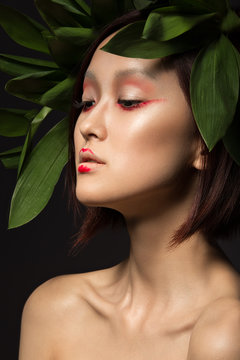 Beautiful Asian girl with a bright make-up art in green leaves. Beauty face. Creative image. 