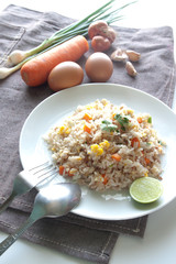 A dish of fried rice, carrot and egg on brown fabric, spoon, fol