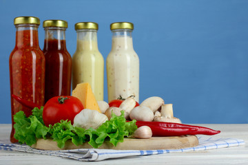 the variety of sauces in glass bottles with tomatoes and fennel with mushrooms on wooden cutting Board with a napkin on a blue wooden background