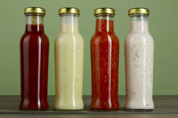 the variety of sauces in glass bottles on a green wooden background