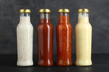 a variety of sauces in glass bottles on a black wooden background