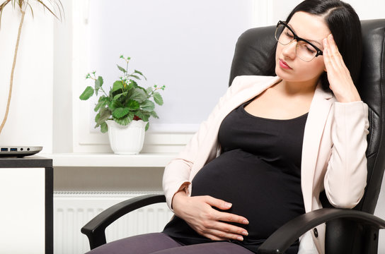 Tired pregnant woman sitting at workplace in the office