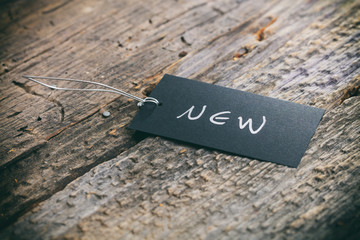 Closeup of pricing tag with twine and "New" text on wooden background