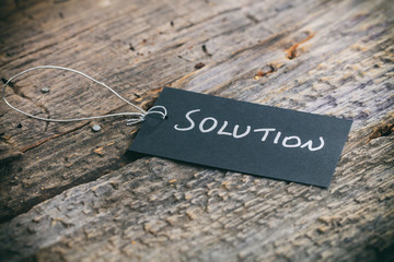 Closeup of pricing tag with twine and "Solution" text on wooden background