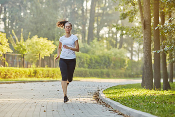 Young woman running in park at sunny summer morning