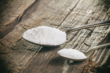 Tablespoon and teaspoon with baking soda, on wooden surface.