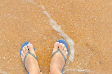 Fototapeta premium Top view close up of man wearing blue flip flops walking along tropical exotic ocean beach