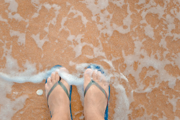 Sea shell and person walking along tropical exotic ocean beach wearing blue flip flops. Top view close up