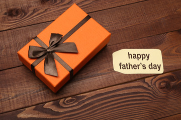 Orange box with brown ribbon on wooden background. Fathers day