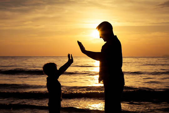 Father and son  playing  on the beach at the sunset time.