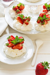 Homemade small strawberry pavlova meringue cakes with mascarpone cream and fresh mint leaves on white plate