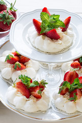 Homemade small strawberry pavlova meringue cakes with mascarpone cream and fresh mint leaves on white plate