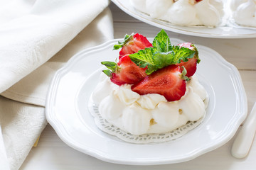Homemade small strawberry pavlova meringue cakes with mascarpone cream and fresh mint leaves on white plate