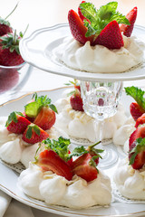 Homemade small strawberry pavlova meringue cakes with mascarpone cream and fresh mint leaves on white plate