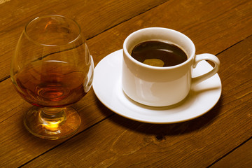 White cup of coffee and cognac in a glass on old wooden table. T