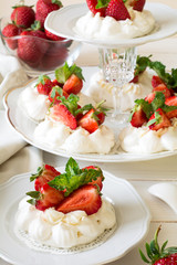 Homemade small strawberry pavlova meringue cakes with mascarpone cream and fresh mint leaves on white plate