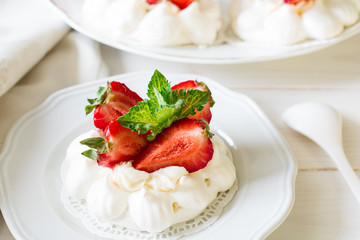 Homemade small strawberry pavlova meringue cakes with mascarpone cream and fresh mint leaves on white plate