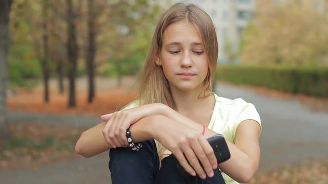 Sad concerned teenage girl waiting for cell phone call outdoor