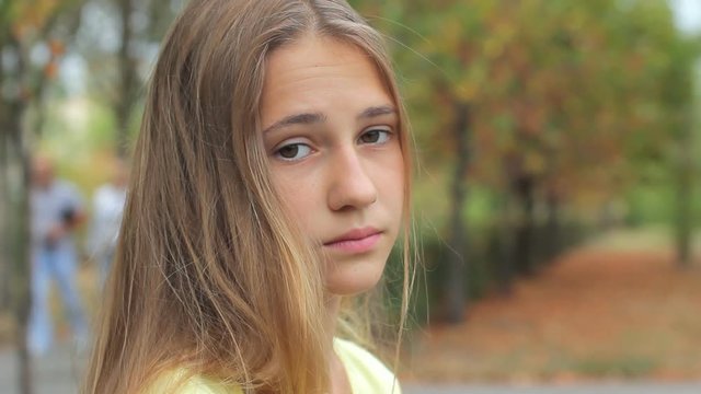 Sad face teenage girl looking at camera outdoors, close up portrait of beautiful young depressed unhappy serious in city park
