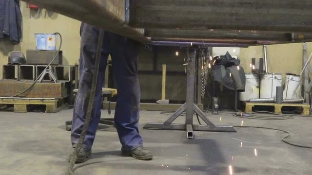 Sparks from welding machine under the table where the worker is welding the part of a metal bar