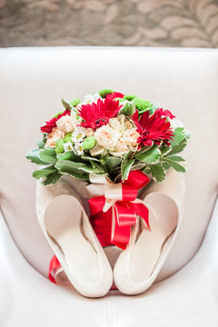 Bouquet with red flowers and shoes on a white leather chair