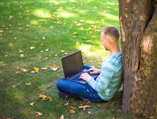 Student using his laptop in autumn city park