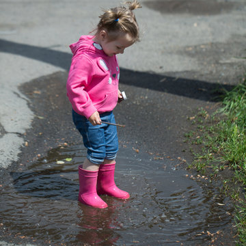 Little girl in rubber boots in buddle