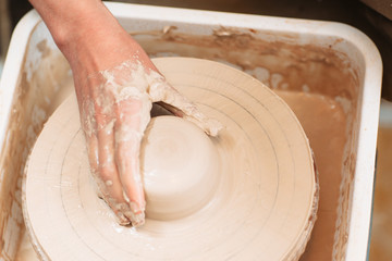 Lump of clay on spinning potters wheel with artisan hand. Top view on process of molding pottery. Close-up on potter hand on lump of clay on pottery wheel.