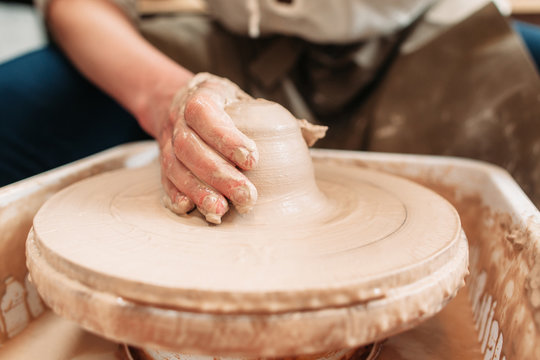 Spinning potters wheel with clay and hand. Close-up of craftsman hand on clay, shaping it into pottery. Dirty potters hand on loam of clay