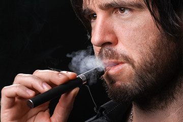 Young man smoking electronic cigarette on black background
