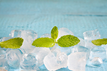 Ice cubes and fresh mint leaves abstract background on blue boards
