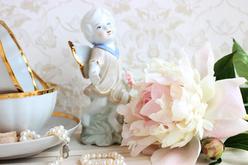 Statuette of an angel on the background with peonies and porcelain cups
