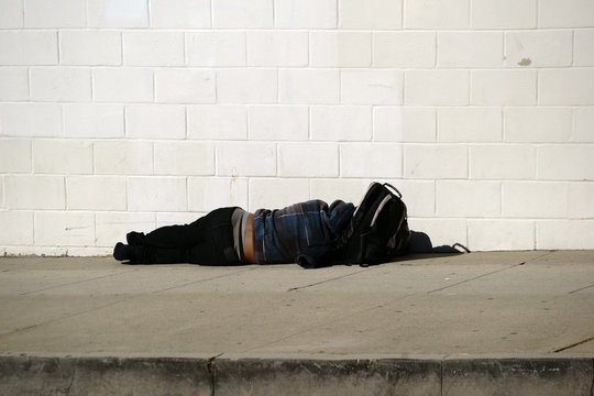 Obdachlos / Ein schwarzer Obdachloser liegt auf dem Gehweg bei sonnigem Wetter.